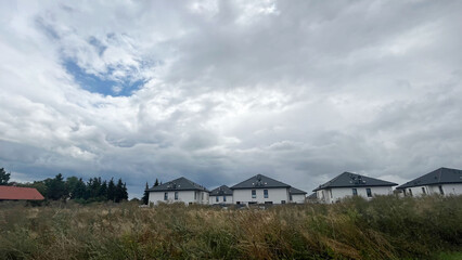 Obraz premium identical white cottages with dark roofs with grass and a sky with rain clouds. village after the rain