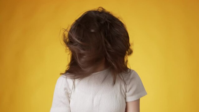 Desperate looking casually dressed young woman ruffling her long dark hair with both hands apparently being agitated against amber background