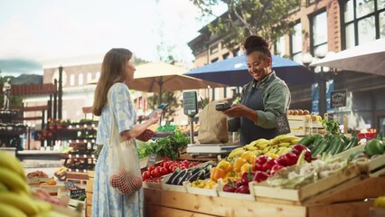 Beautiful Female Customer Buying Sustainable Organic Vegetables From a Joyful Black Female Farmer on a Sunny Summer Day. Successful Street Vendor Managing a Farm Stall at an Outdoors Eco Market - Powered by Adobe
