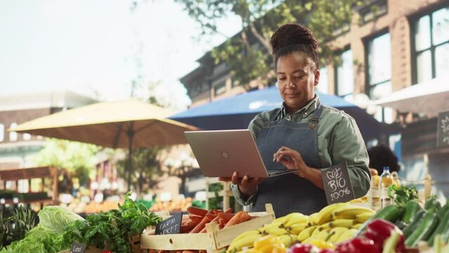 Portrait of a Black Female Running a Street Vendor Food Stand with Fresh Organic Agricultural Products. Farmer Using Laptop Computer to Manage Business Operations, Online Orders and Marketing Campaign