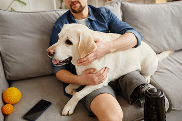 Close up of man with disability holding big white dog in lap while relaxing on couch together