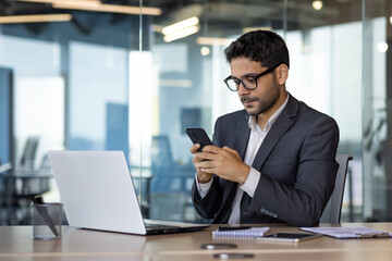 Fototapeta na wymiar Serious thinking businessman using phone at workplace, arab boss in business suit thinking inside office reading online news using app on smartphone.