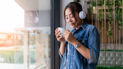 Happy woman wearing jean shirt at coffee corner with a cup of coffee listening music from Bluetooth earphone  is business relaxing concept.