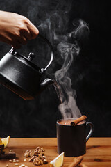 Captured against a dark backdrop, a male hand expertly pours hot tea from a kettle into a classic...