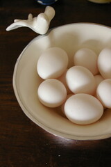 White eggs in a white enamel bowl with a bird motif placed on a wooden table.