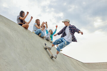 Friends, teengaers meeting at skate park for active leisure time. Boy in casucl clothes skateboarding on ramp. Concept of youth culture, sport, dynamic, extreme, hobby, action and motions, friendship © master1305