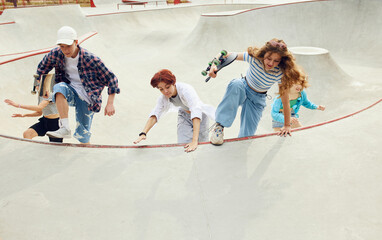 Group of teens in casual clothes, boy and girls running with skate on skateboard ramp. Activity and...