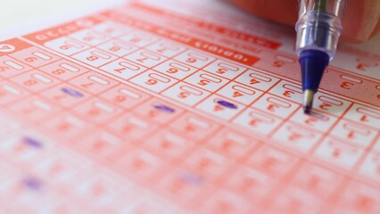 Woman hand marking numbers on Lottery Ticket with Pencil.