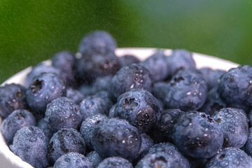 Macro photography of fresh antioxidant natural blueberries in a white bowl. Close-up of ripe blueberries on a green background. Concept of healthy eating.