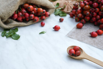 Rose hip in wooden spoon on a white marble background. Healthy ingredient. Alternative medicine and herbal therapy concept. Side view, copy space.
