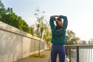 Rear view of attractive female runner stretching her arms before her early morning exercise