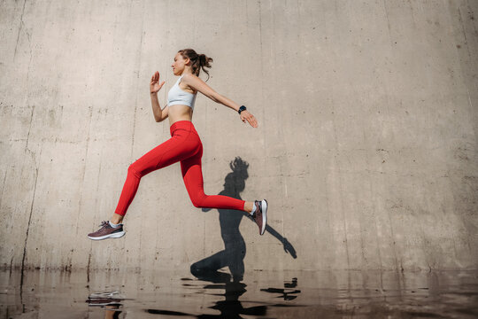 Fitness woman running in front of concrete wall casting shadow. © Halfpoint