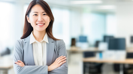 Confident young asian businesswoman smiling while standing with crossed arms at office. Perfect business lady. Beautiful young businesswoman looking at camera.  - obrazy, fototapety, plakaty