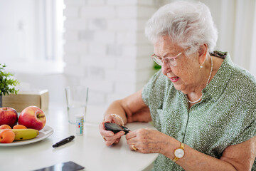 Diabetic senior patient checking her blood sugar level with fingerstick testing glucose meter.