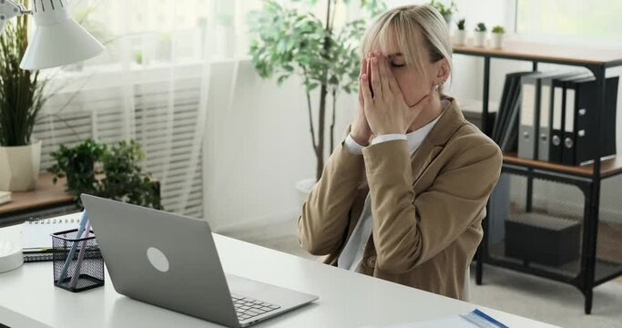 Weary Caucasian businesswoman is shown yawning and massaging her neck while at her workplace. The signs of fatigue are evident as she takes a moment to relieve tension and fatigue from her busy day.