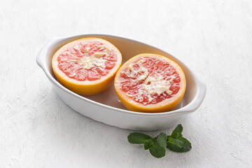 White ceramic baking dish red grapefruit halves smeared with butter on a light gray table. Cooking step, cooking delicious dessert