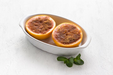 White ceramic baking dish with red grapefruit halves smeared with butter and sprinkled with sugar and cinnamon on a light gray table. Cooking step, cooking delicious dessert