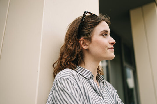 Young Woman with Glasses Leaning Against Modern Building and Looking Sideways