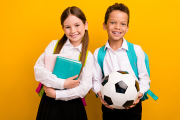 Photo of two lovely schoolkids prepare for school year hold soccer ball textbooks isolated on...
