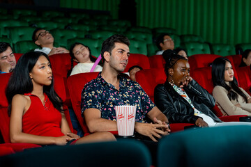 Group of multiethic people sit on seats in cinema theater and they look boring during watch movie...