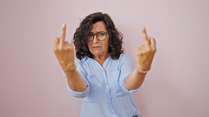 Middle age hispanic woman standing with angry expression doing middle finger gesture over isolated pink background