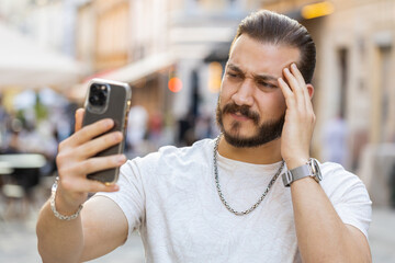 Bearded young man use smartphone typing browsing, loses becoming surprised sudden lottery results,...