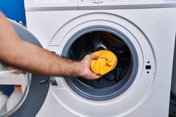Young hispanic man putting clothes on washing machine at laundry room