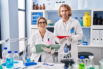 Two people working at scientist laboratory smiling and laughing hard out loud because funny crazy...
