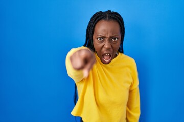 Beautiful black woman standing over blue background pointing displeased and frustrated to the...