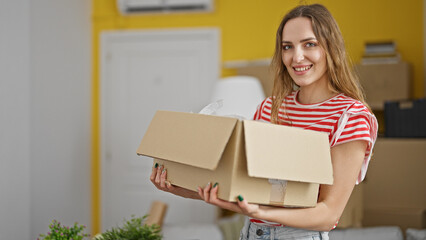 Young blonde woman smiling confident holding package at new home