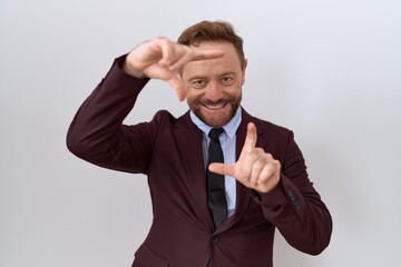 Middle age business man with beard wearing suit and tie smiling making frame with hands and fingers with happy face. creativity and photography concept.