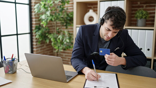 Young hispanic man business worker wearing headset on a video call using credit card at office