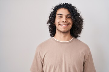 Hispanic man with curly hair standing over white background with a happy and cool smile on face. lucky person.