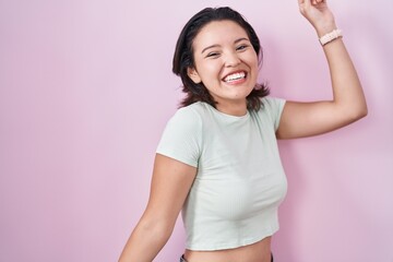 Hispanic young woman standing over pink background dancing happy and cheerful, smiling moving casual and confident listening to music