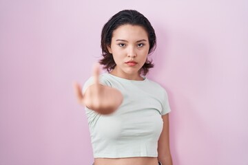 Hispanic young woman standing over pink background showing middle finger, impolite and rude fuck off expression