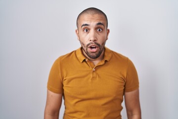 Hispanic man with beard standing over white background afraid and shocked with surprise and amazed expression, fear and excited face.