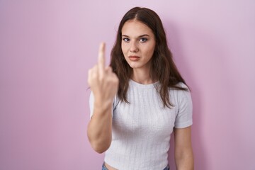Young hispanic girl standing over pink background showing middle finger, impolite and rude fuck off expression