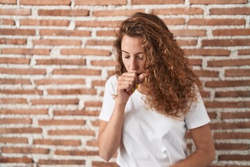 Young caucasian woman standing over bricks wall background feeling unwell and coughing as symptom for cold or bronchitis. health care concept.