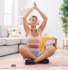 Fototapeta na wymiar Young blonde woman doing yoga exercise sitting on floor at home