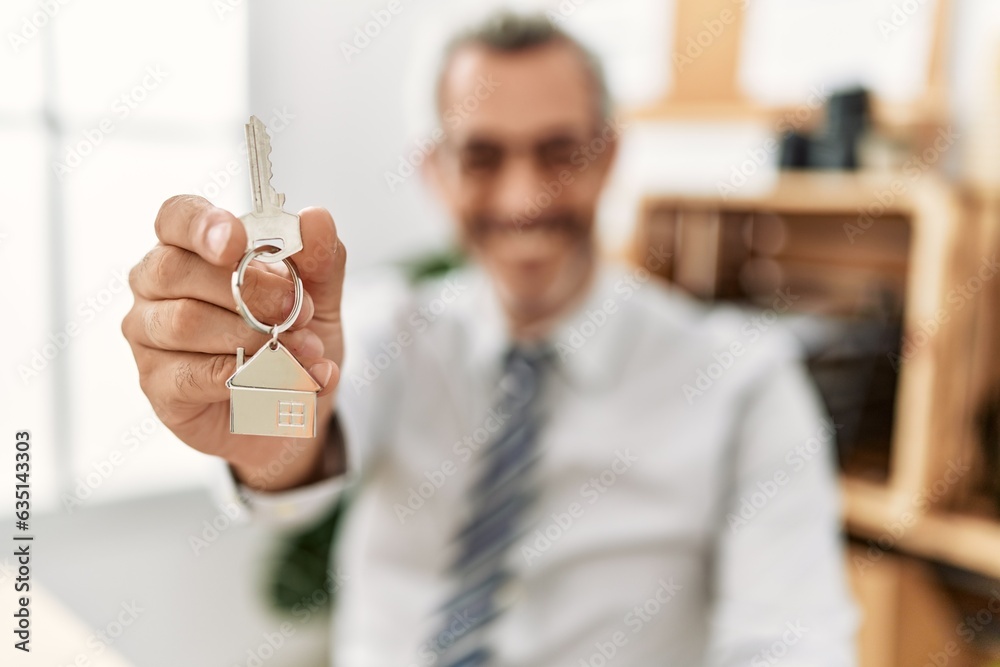 Sticker middle age grey-haired man real state agent holding key of new home at office