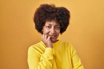 Obraz na płótnie Canvas Young african american woman standing over yellow background looking stressed and nervous with hands on mouth biting nails. anxiety problem.