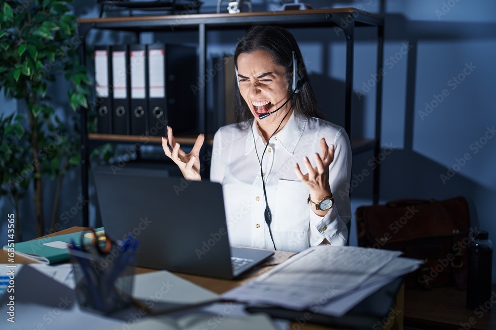 Canvas Prints young brunette woman wearing call center agent headset working late at night crazy and mad shouting 