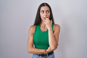 Young woman standing over isolated background looking stressed and nervous with hands on mouth biting nails. anxiety problem.