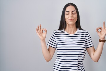 Young brunette woman wearing striped t shirt relaxed and smiling with eyes closed doing meditation gesture with fingers. yoga concept.