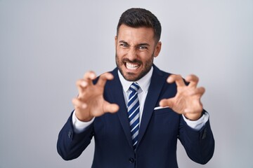 Handsome hispanic man wearing suit and tie smiling funny doing claw gesture as cat, aggressive and sexy expression