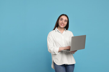Smiling young woman with laptop on light blue background. Space for text