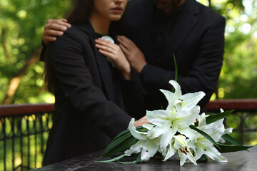 People near white lilies on tombstone at cemetery, closeup. Funeral ceremony