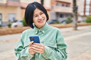 Young chinese woman smiling confident using smartphone at street