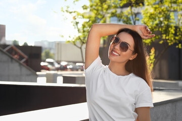 Beautiful smiling woman in sunglasses on city street, space for text