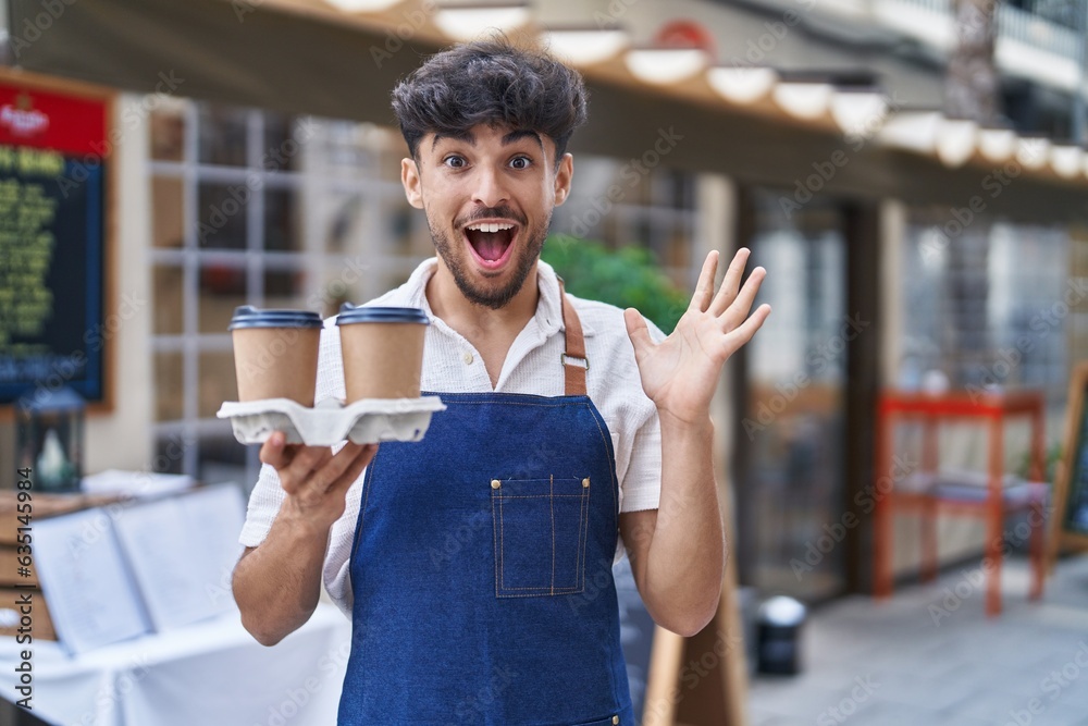 Wall mural arab man with beard wearing waiter apron at restaurant terrace celebrating victory with happy smile 